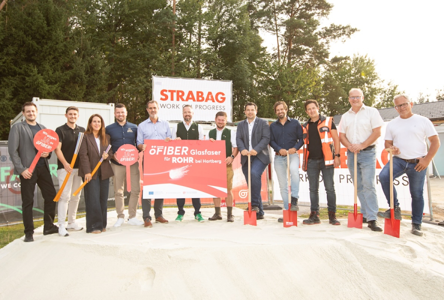 12 Personen stehen auf Sand für den Spartenstich, mit einem Schild auf dem steht "öFIBER Glasfaser für Rohr am Hartberg"