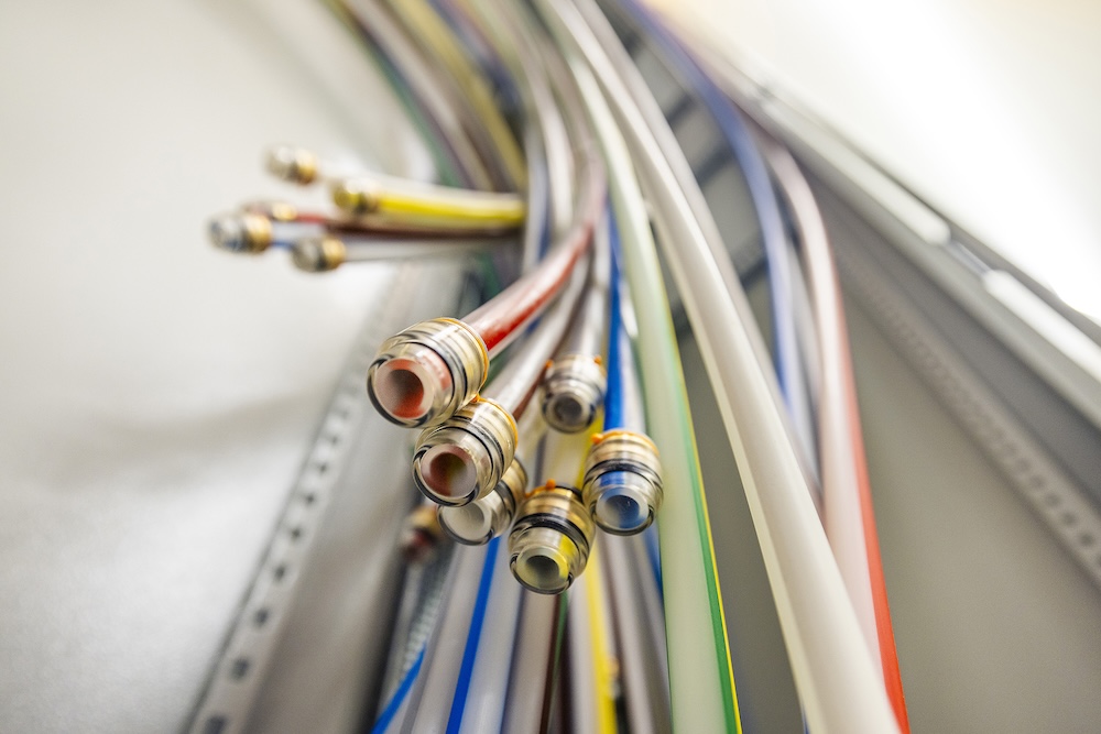 Nahaufnahme ordentlich angeordneter, farbenfroher Koaxialkabel mit Metallsteckern, die aus einer Wand herausragen.